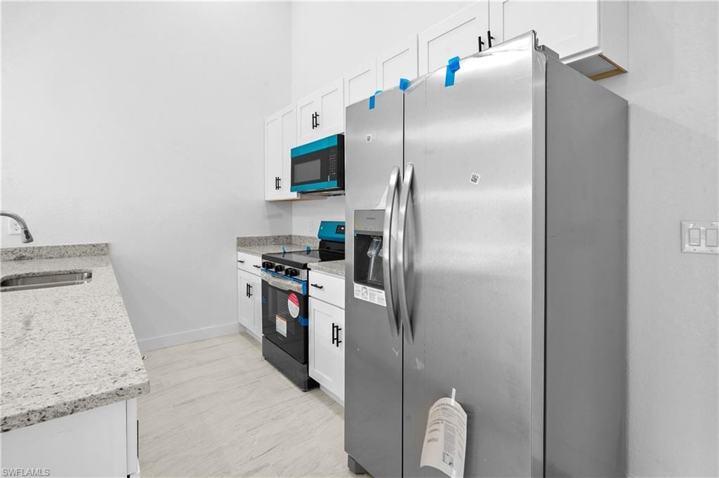 Kitchen with stainless steel refrigerator with ice dispenser, white cabinets, electric range, and light stone counters