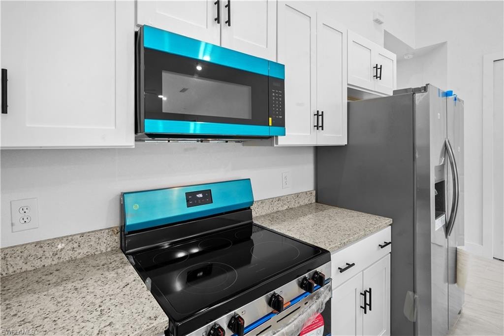 Kitchen featuring stainless steel appliances, light stone countertops, and white cabinets
