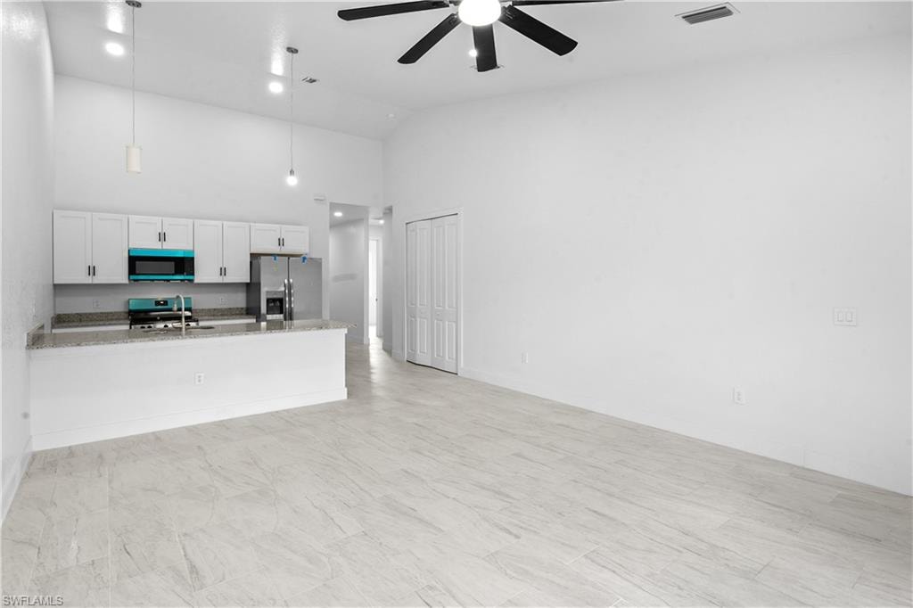 Kitchen with appliances with stainless steel finishes, white cabinetry, decorative light fixtures, light stone counters, and open floor plan