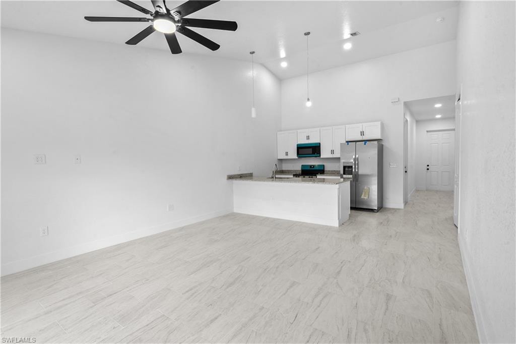 Kitchen with a peninsula, black appliances, white cabinets, a towering ceiling, and open floor plan