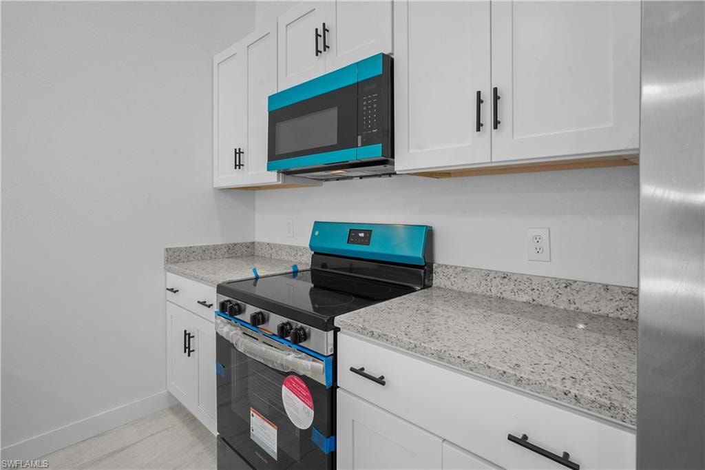 Kitchen featuring stainless steel electric range oven, white cabinetry, light stone countertops, and light wood-type flooring