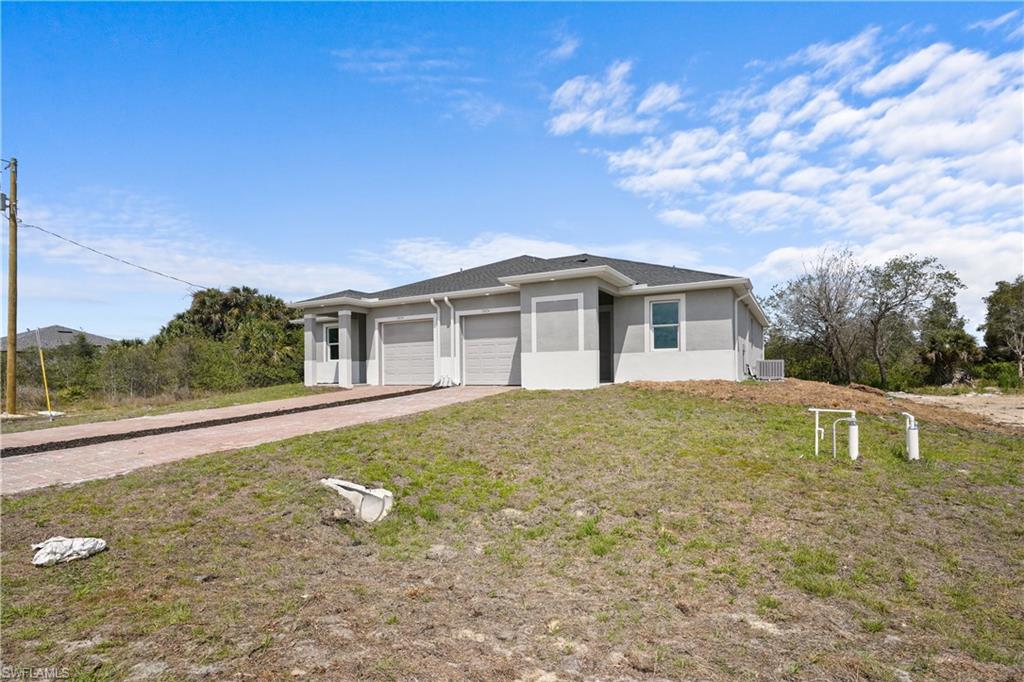 Prairie-style home with driveway, stucco siding, a garage, and a front lawn