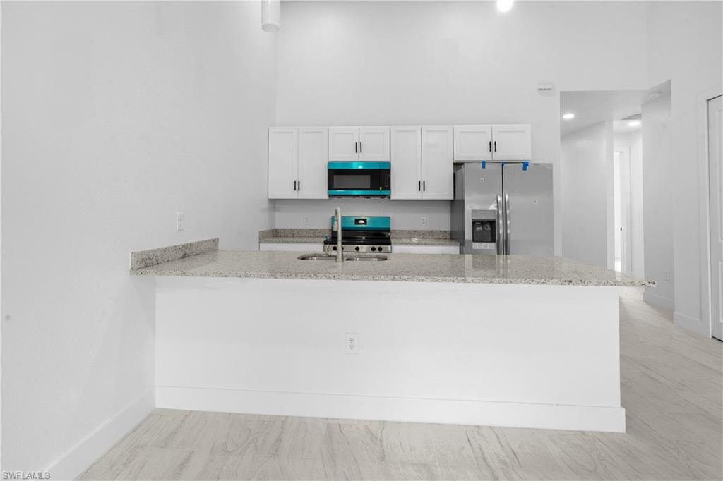 Kitchen featuring light stone counters, white cabinetry, appliances with stainless steel finishes, a peninsula, and a high ceiling