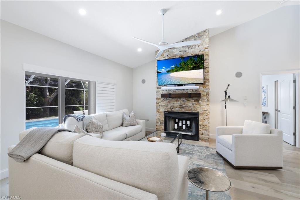 Living room with a stone fireplace, ceiling fan, light hardwood / wood-style floors, and high vaulted ceiling