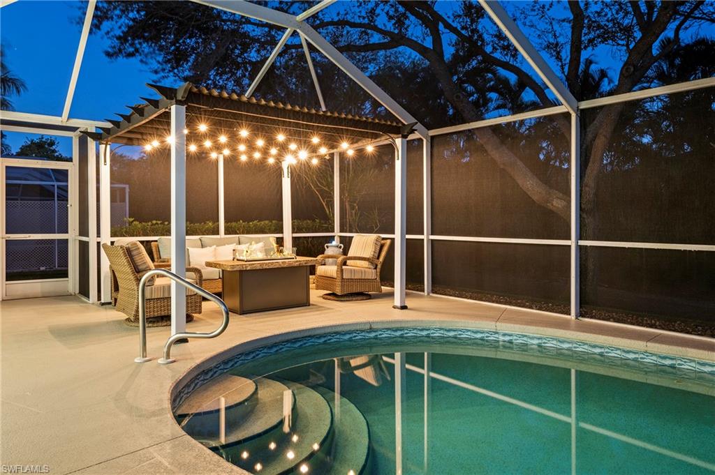 Pool at night featuring an outdoor living space with a fire pit, glass enclosure, and a patio area