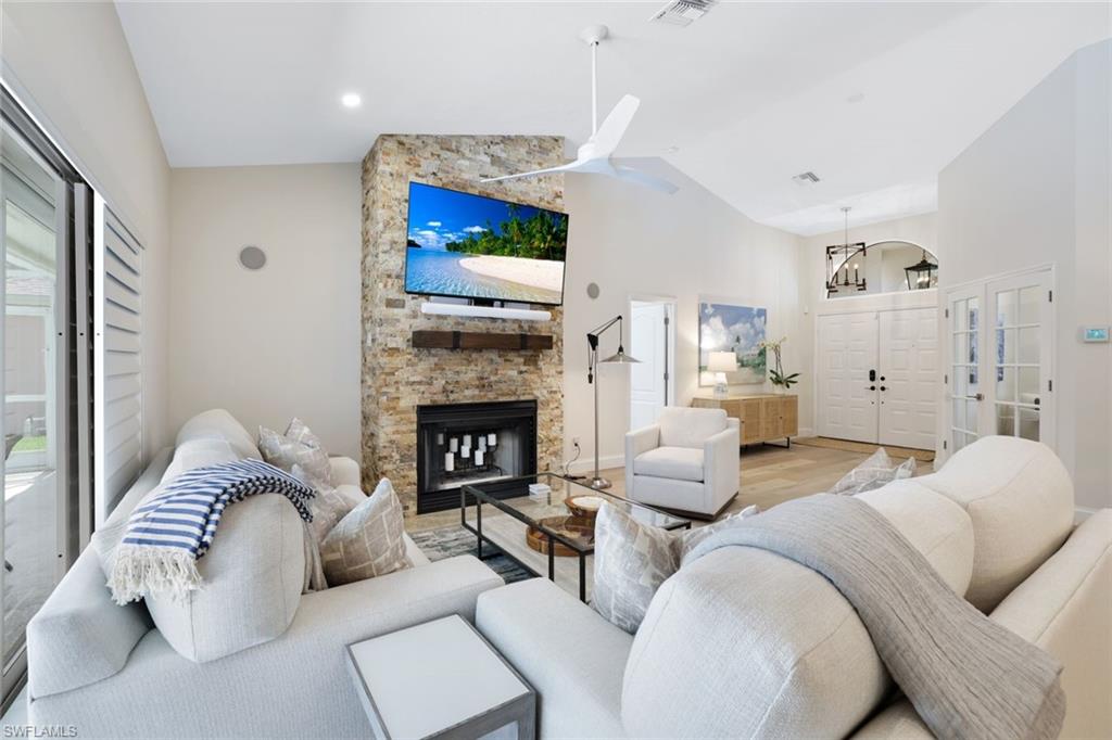 Living room featuring french doors, light hardwood / wood-style flooring, ceiling fan, a fireplace, and high vaulted ceiling