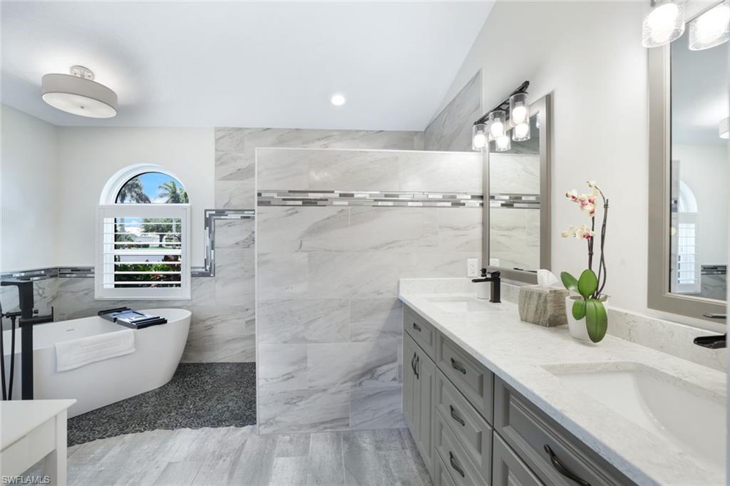 Bathroom with double vanity, tile walls, tile patterned floors, and a tub