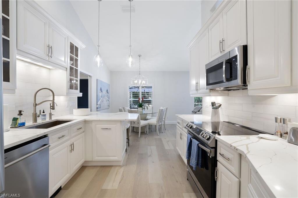 Kitchen featuring appliances with stainless steel finishes, tasteful backsplash, sink, light wood-type flooring, and white cabinetry