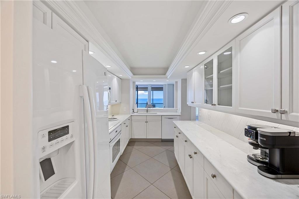 Kitchen with white appliances, white cabinetry, glass insert cabinets, light tile patterned floors, and light stone counters
