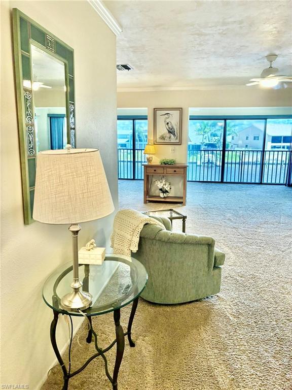 Carpeted living room featuring a ceiling fan and ornamental molding