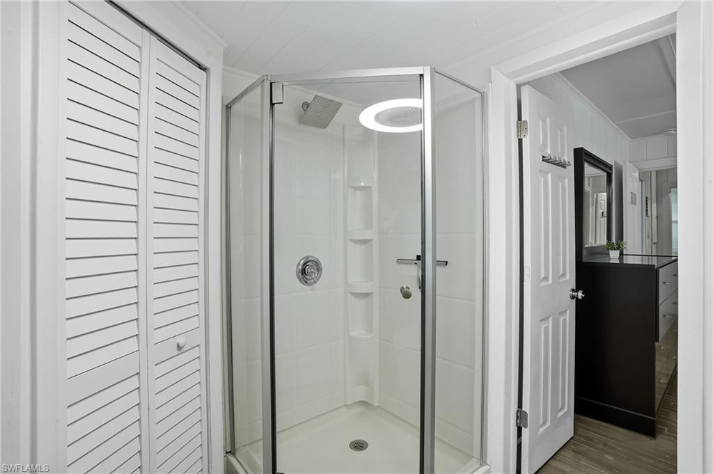 Bathroom featuring a closet, a shower stall, wood finished floors, and ornamental molding - Virtually Edited Image