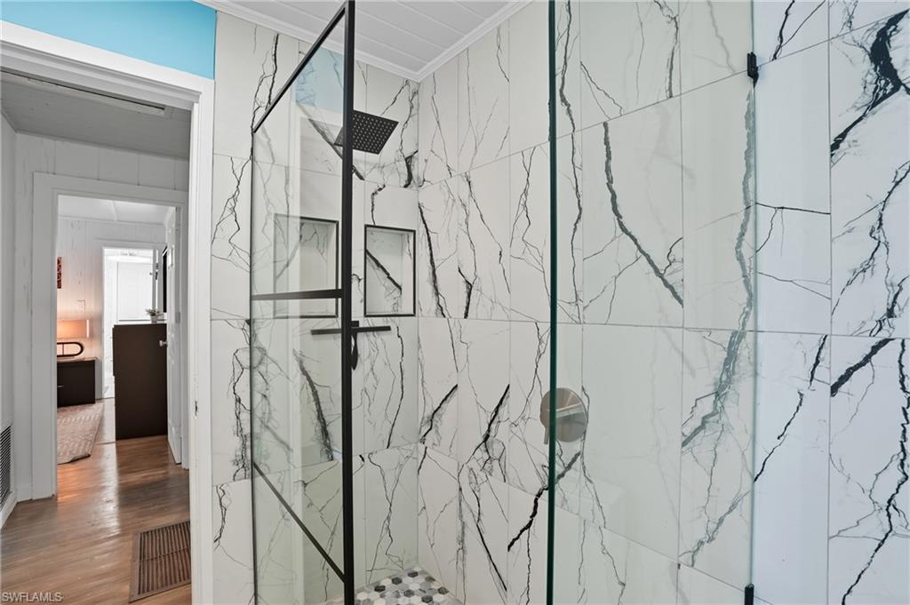 Full bathroom with a marble finish shower, wood finished floors, and ornamental molding - Virtually Edited Image