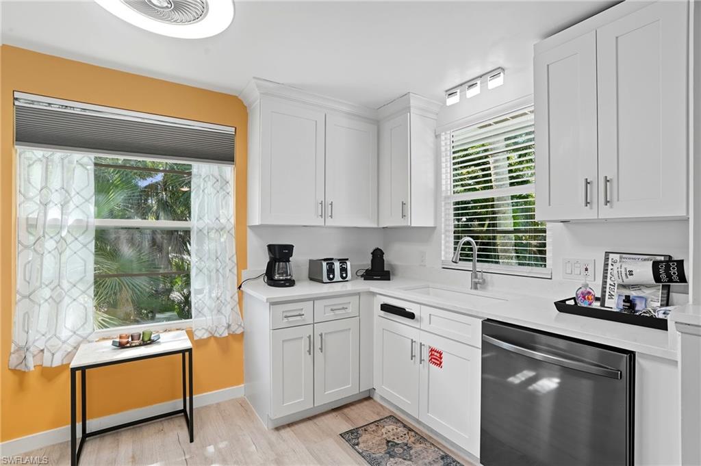 Kitchen featuring stainless steel dishwasher, white cabinets, light wood-style flooring, and light stone countertops - Virtually Edited Image