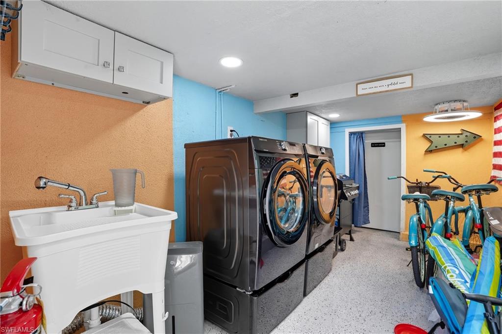 Laundry area with cabinet space, separate washer and dryer, dark aggregate flooring, a textured wall, and recessed lighting - Virtually Edited Image