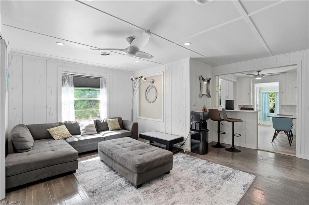 Living room featuring a ceiling fan, dark wood-style flooring, recessed lighting, and wooden walls - Virtually Edited Image