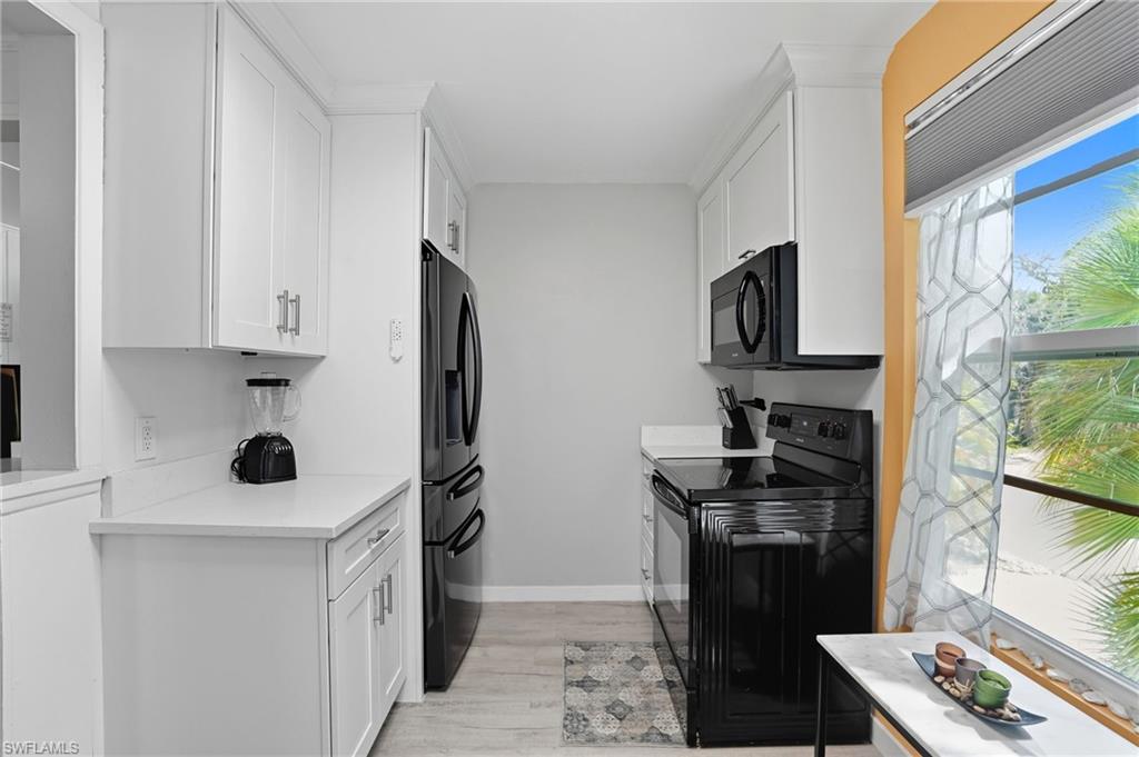 Kitchen featuring black appliances, white cabinets, and light wood-style floors - Virtually Edited Image