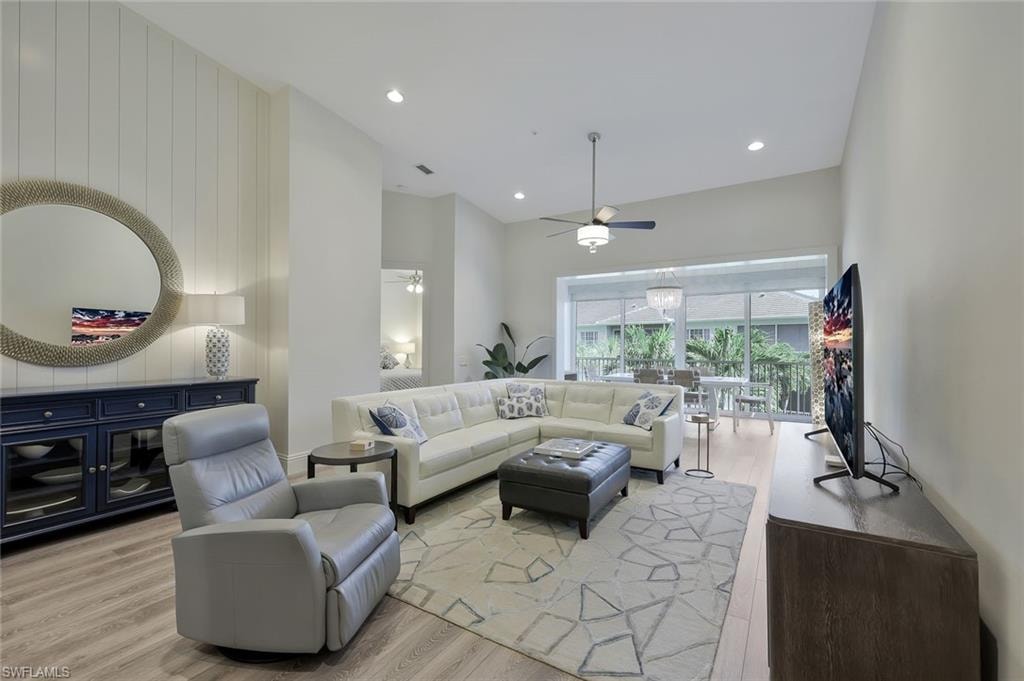 Living room with ceiling fan, light wood-style flooring, recessed lighting, a high ceiling, and wooden walls