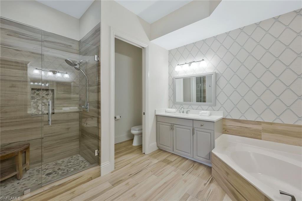 Full bathroom featuring a bath, a shower stall, vanity, and light wood-style flooring