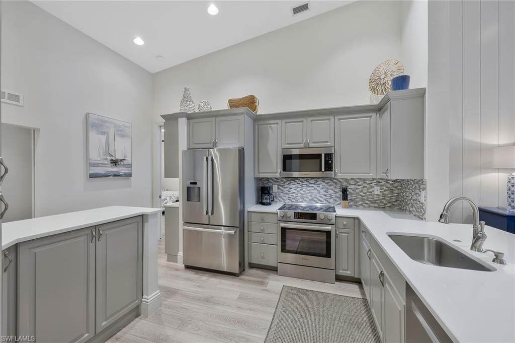 Kitchen featuring gray cabinetry, appliances with stainless steel finishes, light wood-type flooring, backsplash, and recessed lighting