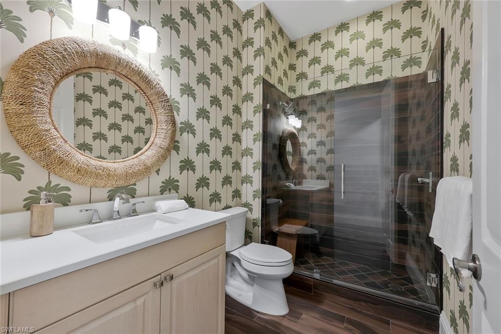Bathroom featuring vanity, wood finish floors, a stall shower, and wallpapered walls