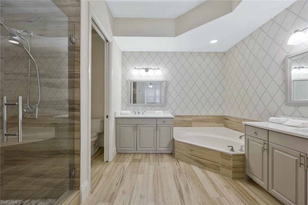 Bathroom with tile walls, a stall shower, two vanities, a garden tub, and recessed lighting