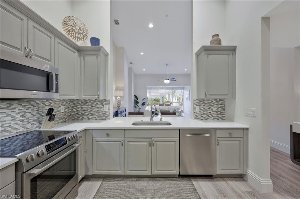 Kitchen featuring stainless steel appliances, light wood-style floors, ceiling fan, backsplash, and light stone counters