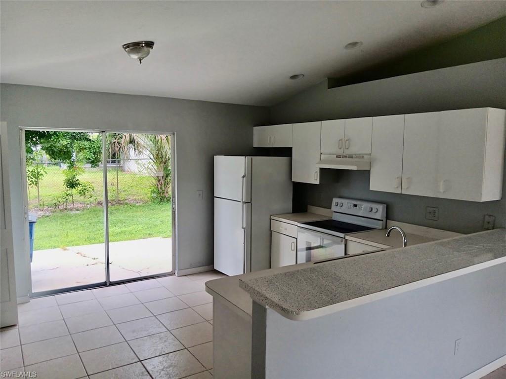 Kitchen featuring white appliances, light tile patterned floors, vaulted ceiling, white cabinets, and light countertops
