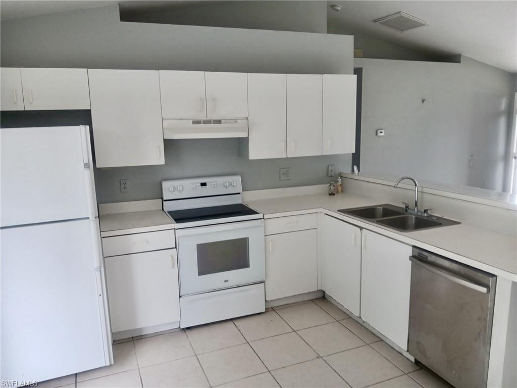 Kitchen with white appliances, light countertops, light tile patterned flooring, and vaulted ceiling