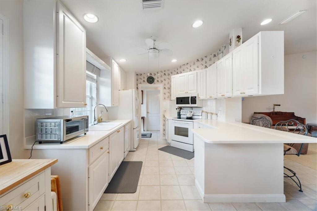 Kitchen with light countertops, white appliances, a kitchen bar, white cabinetry, and light tile patterned floors