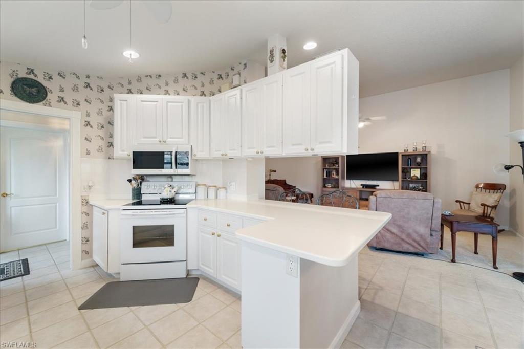 Kitchen with white appliances, ceiling fan, a peninsula, light countertops, and white cabinets