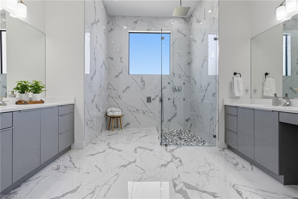 Bathroom with light marble finish flooring, a marble finish shower, and two vanities