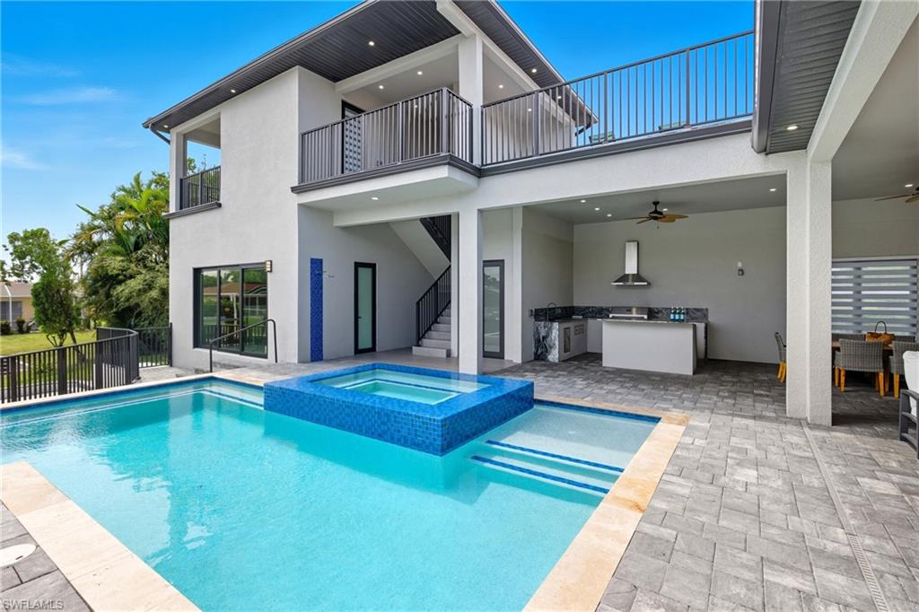 Rear view of house featuring a patio, stucco siding, an outdoor kitchen, a ceiling fan, and a pool with connected hot tub