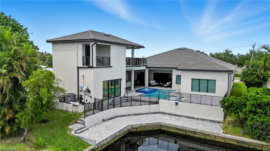 Back of house with a patio area, stucco siding, a balcony, a fenced backyard, and a pool with connected hot tub