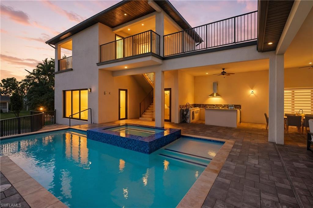 View of pool featuring a patio, area for grilling, a pool with connected hot tub, a balcony, and stairway