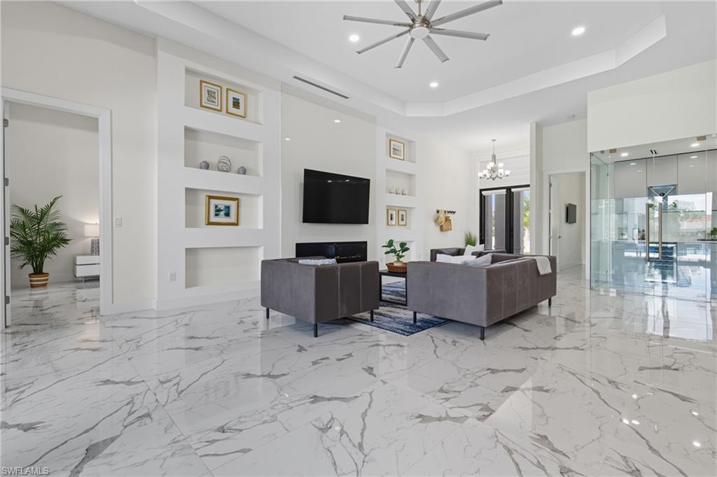 Living area featuring built in features, a tray ceiling, a chandelier, light marble finish floors, and recessed lighting