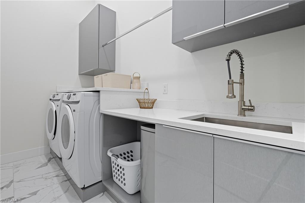 Laundry area featuring light marble finish floors, cabinet space, and washing machine and clothes dryer