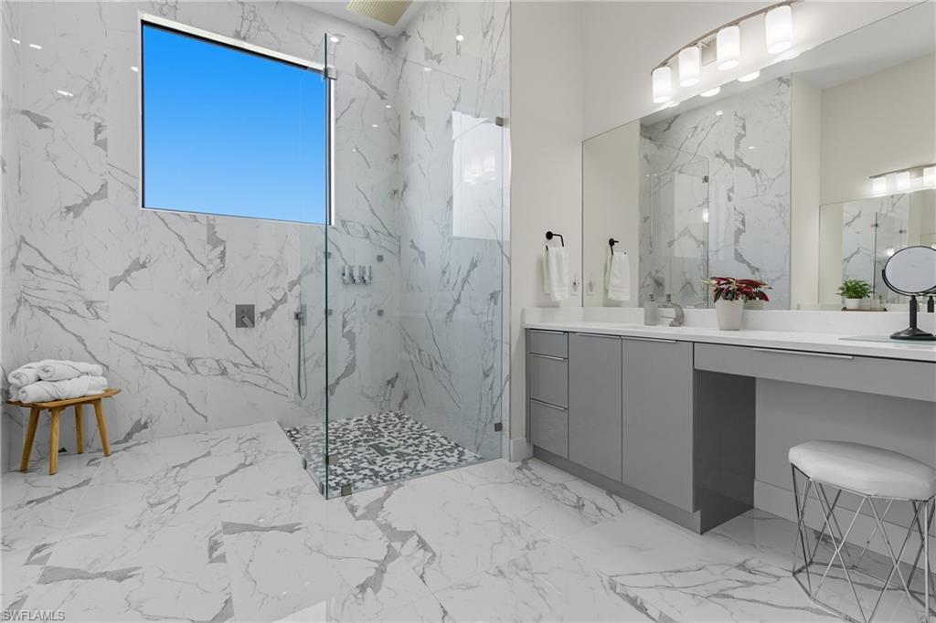 Bathroom featuring light marble finish flooring, a marble finish shower, vanity, stone wall, and tile walls