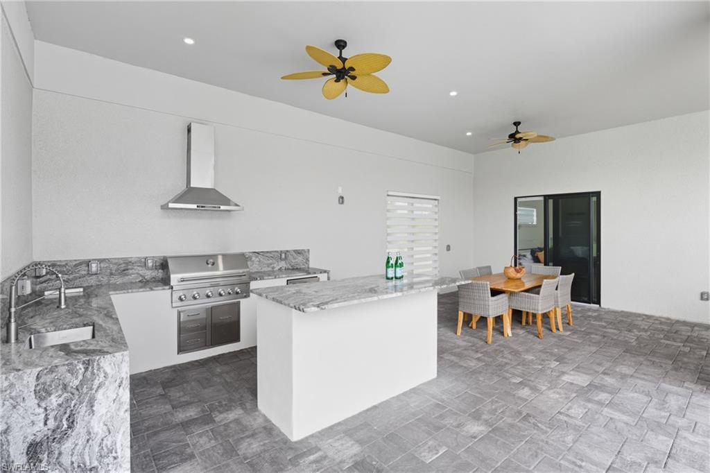 Kitchen with light stone countertops, wall chimney range hood, a ceiling fan, recessed lighting, and white cabinets
