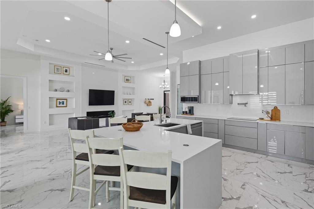Kitchen with gray cabinets, a kitchen bar, pendant lighting, a raised ceiling, and recessed lighting