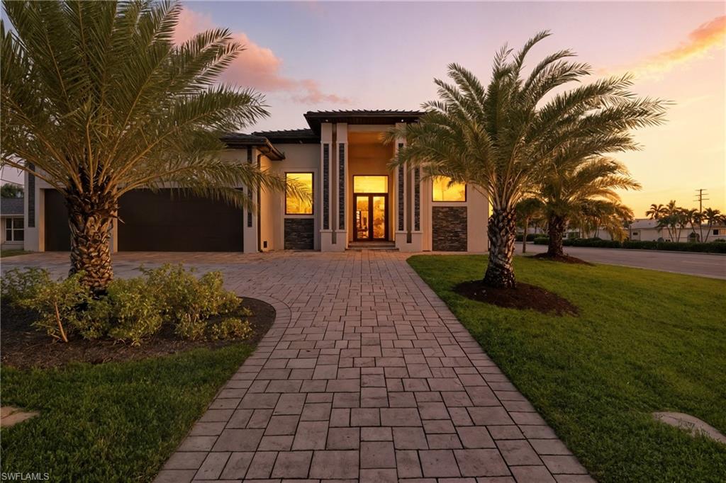 Contemporary style home with decorative driveway, a tiled roof, a yard, stucco siding, and an attached 3 car garage