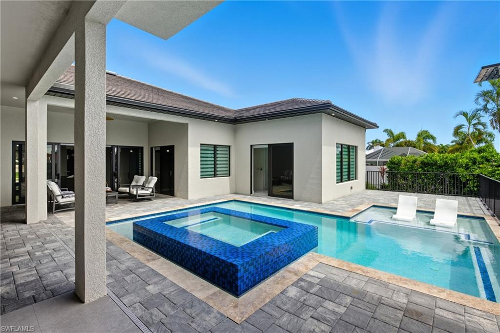 Rear view of property featuring a patio, a pool with connected hot tub, and stucco siding