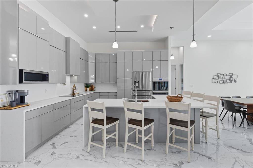 Kitchen featuring gray cabinets, modern cabinets, a kitchen breakfast bar, light marble finish floors, and hanging light fixtures