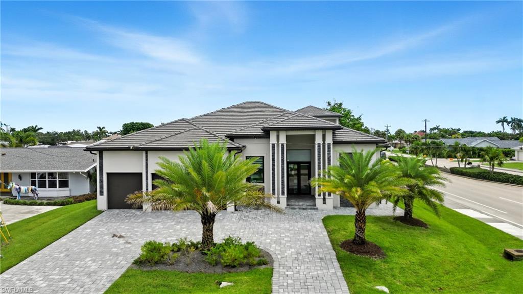 View of front of house with a front yard, stucco siding, decorative driveway, a garage, and a tiled roof