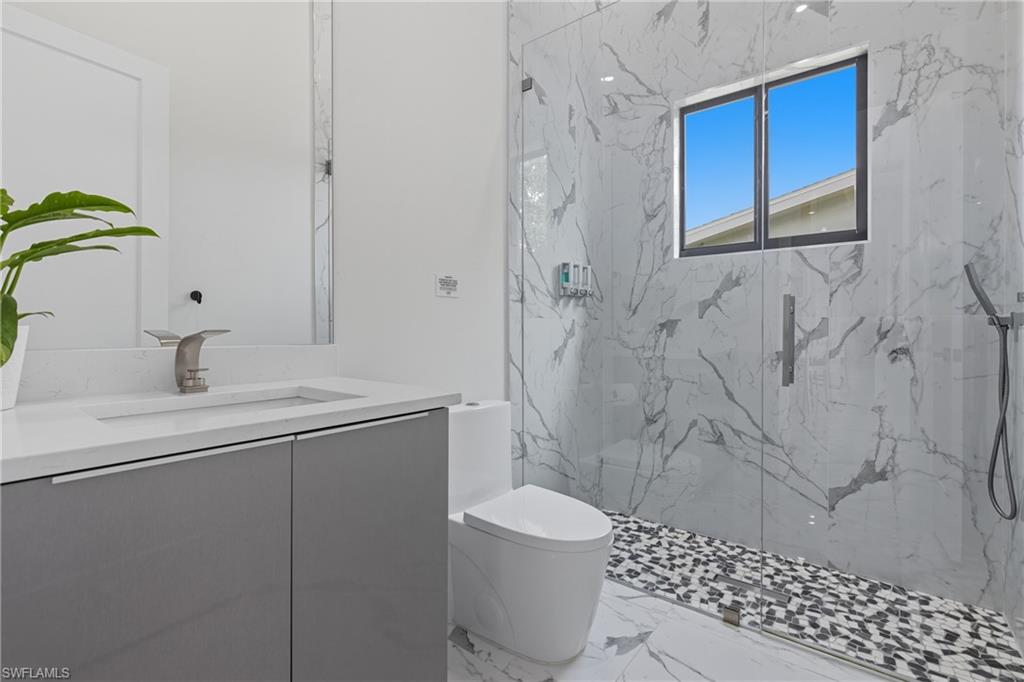 Full bath featuring vanity, a marble finish shower, and light marble finish floors