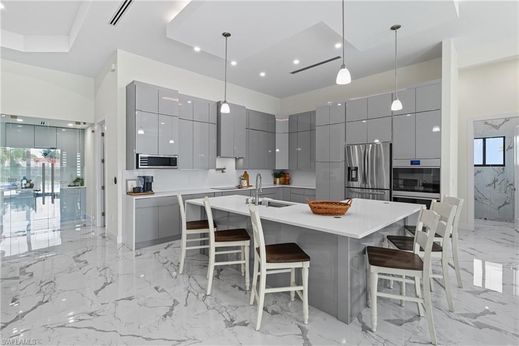 Kitchen featuring gray cabinets, pendant lighting, light marble finish floors, modern cabinets, and a breakfast bar