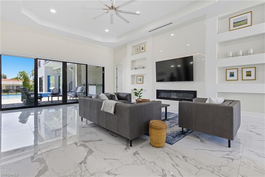 Living room featuring built in shelves, light marble finish flooring, recessed lighting, and a tray ceiling