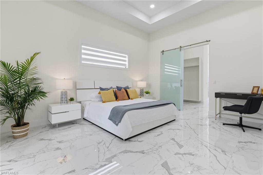 Bedroom featuring a walk in closet, light marble finish floors, a barn door, recessed lighting, and a tray ceiling