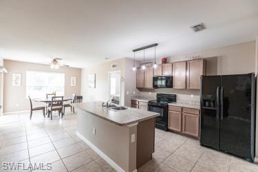 Kitchen with black appliances, pendant lighting, light countertops, light tile patterned flooring, and a center island with sink