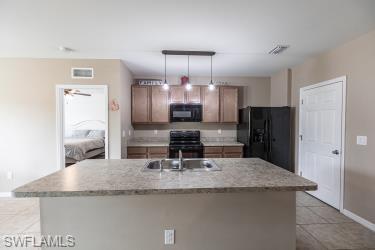 Kitchen featuring light countertops, black appliances, a kitchen island with sink, light tile patterned floors, and decorative light fixtures