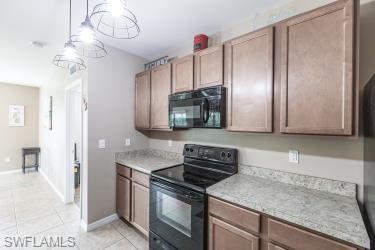 Kitchen featuring black appliances, light tile patterned floors, and decorative light fixtures